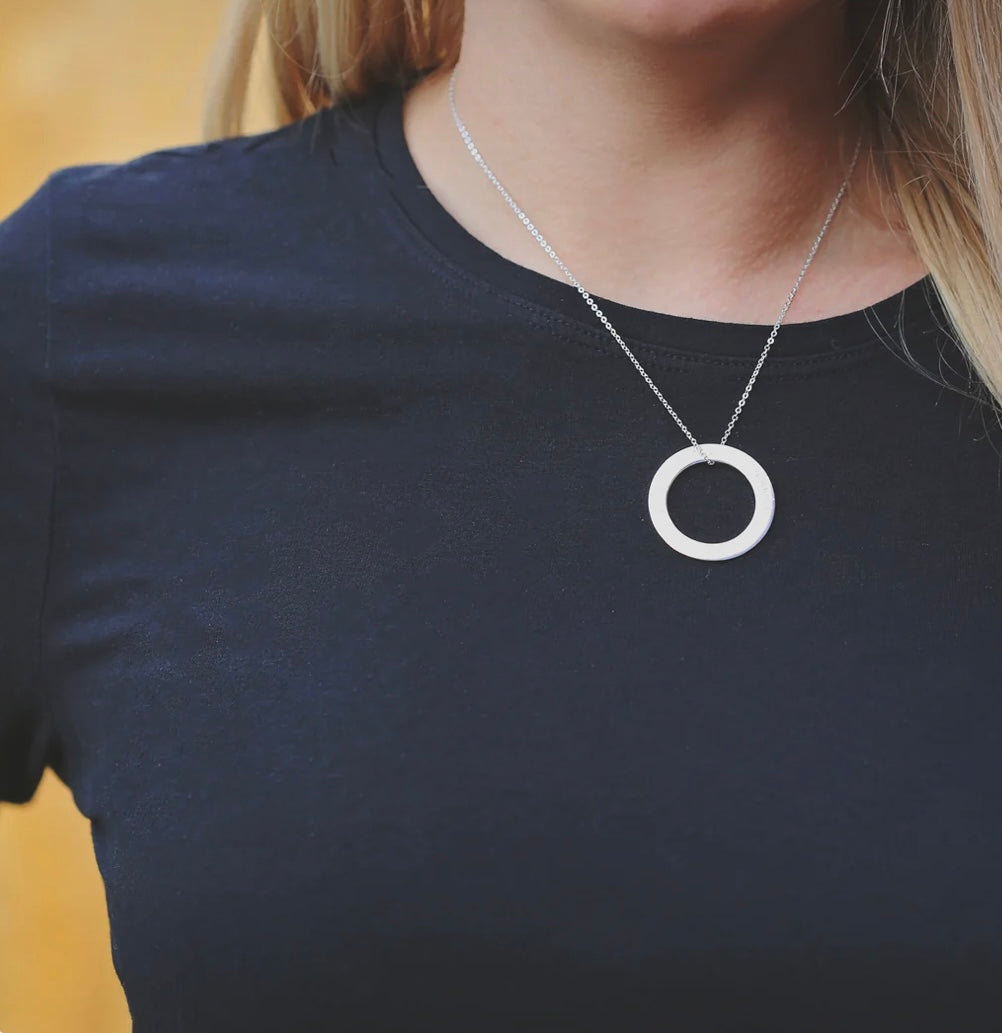 Person wearing a necklace with a circular pendant on a plain background
